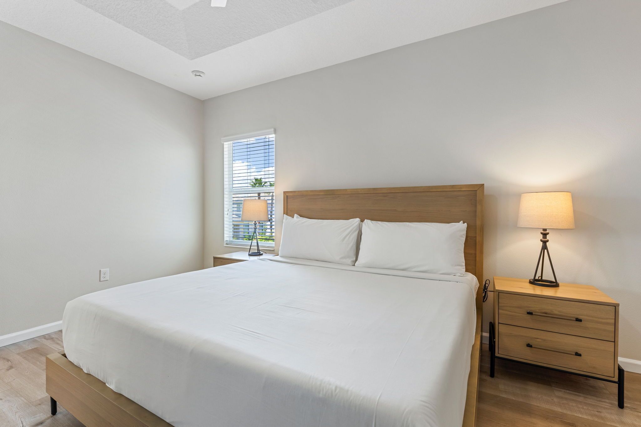 A bedroom with a large bed, a bedside table with a lamp, and a window with blinds.