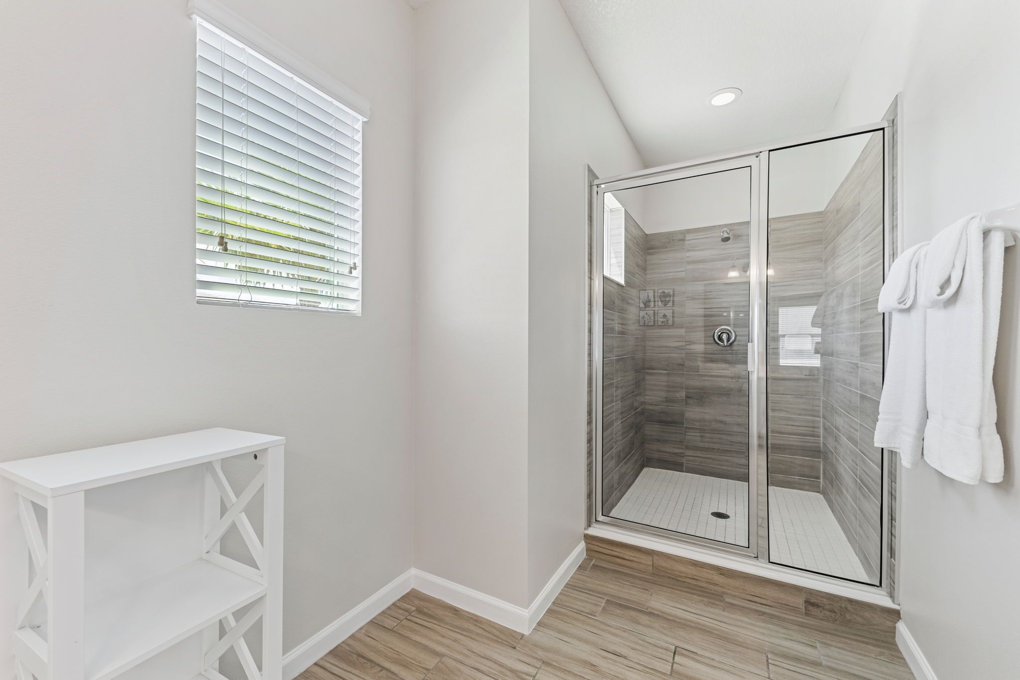 A modern bathroom with a glass-enclosed shower, a white vanity, and a window with blinds.