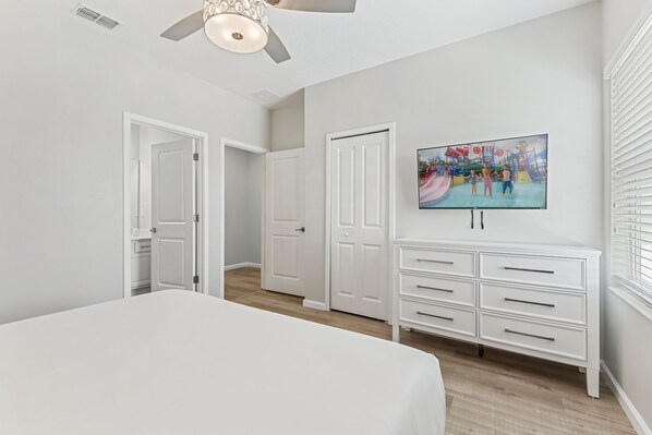 A bedroom with a bed, a ceiling fan, a white dresser, and a painting of a water park. - 2605 Yountville Avenue (Kissimmee)