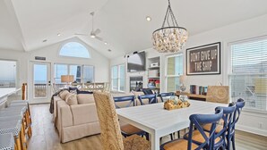A spacious dining area with a white table and blue chairs, a cozy seating area with a sofa, and a kitchen in the background.