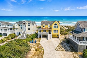 A beachfront property with multiple houses, a central yellow house with a porch, and a view of the ocean.