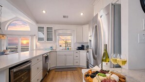 A modern kitchen with a view of the sunset, a stainless steel refrigerator, and a charcuterie board.