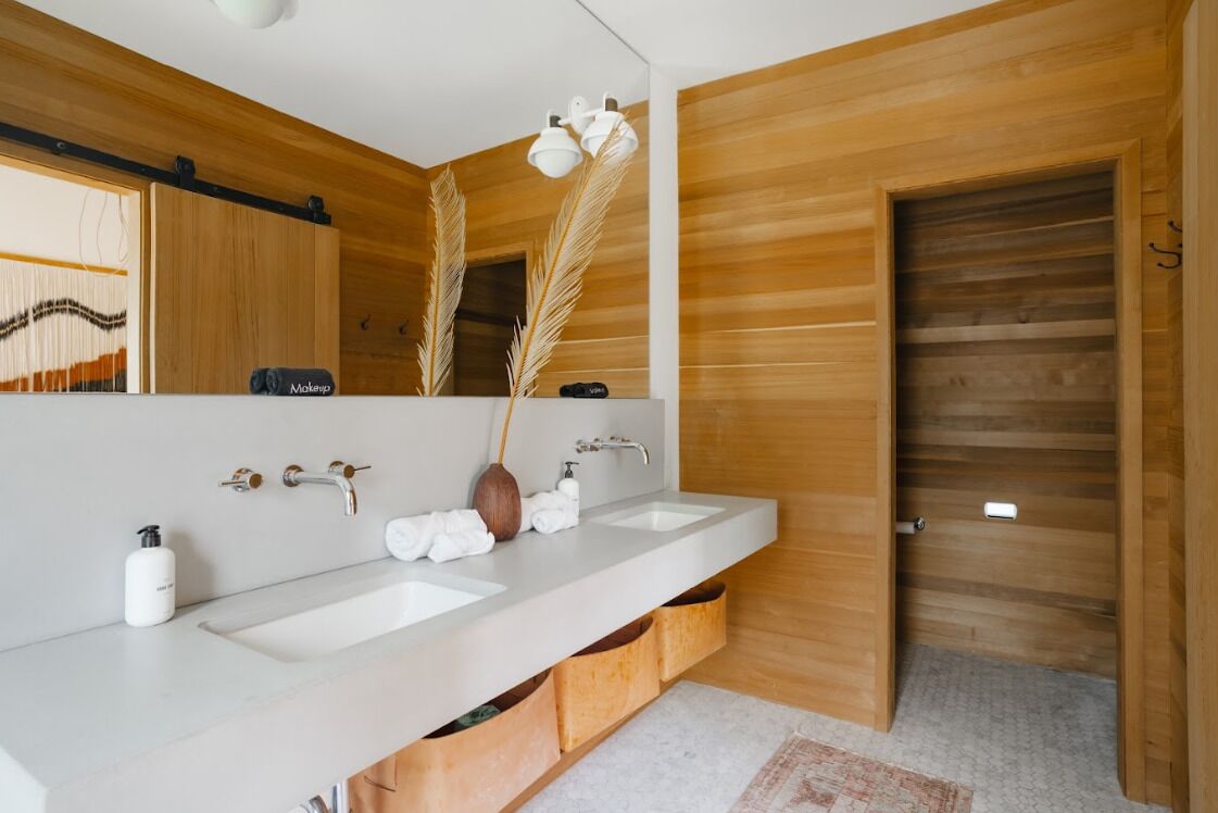 Een moderne badkamer met houten lambrisering, een grote spiegel, twee wastafels en een handdoekrek.