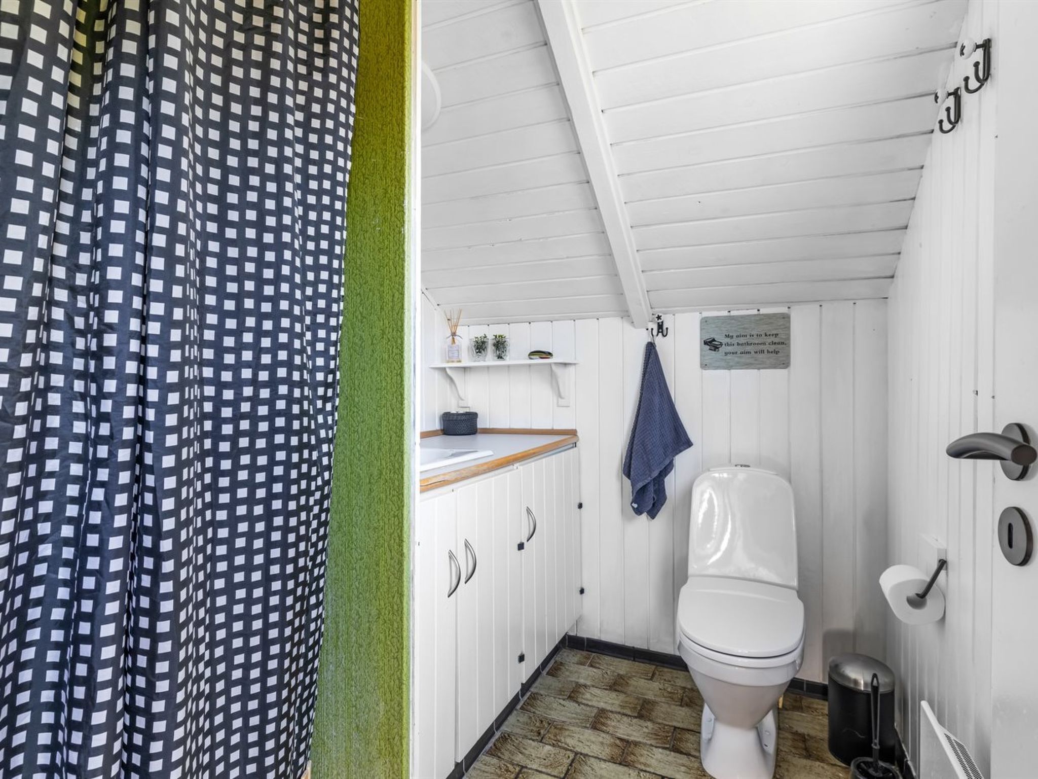 A compact bathroom with a white toilet, a small shelf with toiletries, and a sign on the wall.