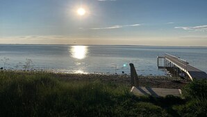 Un muelle de madera se adentra en aguas tranquilas, con un cielo despejado y el sol bajo en el horizonte.