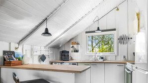 Una cocina moderna con armarios blancos, encimera de madera, un taburete, una cafetera y una ventana con vistas a árboles.