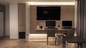 A modern hotel room with a wooden desk, two monitors, a television, and a dining area. - 21heritage hotel (Wonju)