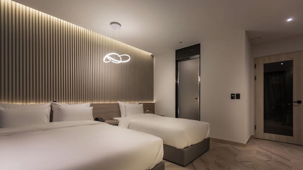 A modern hotel room with two beds, a wooden slat wall, a ceiling light, and a door. - 21heritage hotel (Wonju)