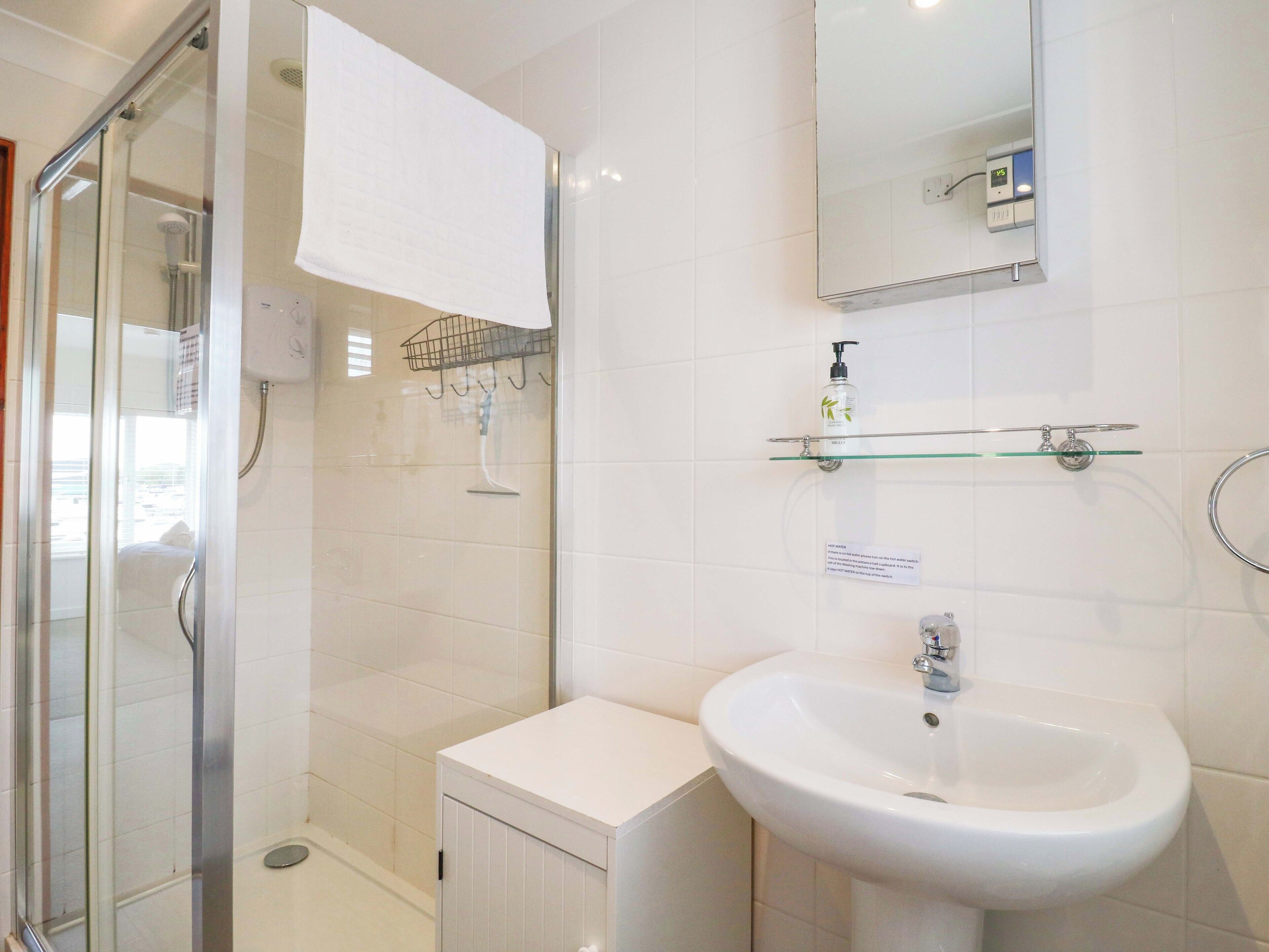 A modern bathroom with a glass shower enclosure, a white sink, and a mirror above it.