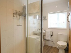 Ein modernes Badezimmer mit einer Duschkabine, einem weißen Waschbecken, einer Toilette und einem Fenster mit Jalousien.