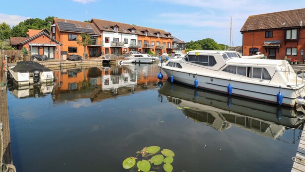 A marina with boats docked, surrounded by residential buildings with red and white facades. - Kingsmere (Norwich)