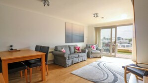 A modern living room with a wooden dining table, grey sofas, and a view of boats through a large glass door. - Kingsmere (Norwich)