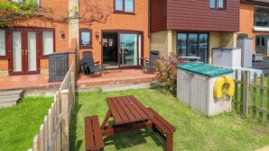 A two-story house with a patio, a wooden table, and a hot tub. - Kingsmere (Norwich)
