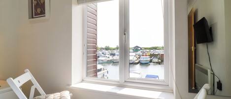 A room with a large window overlooking a marina, a bed with a blue blanket, and a white chair.