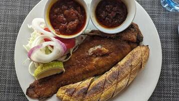 A plate with a whole fried fish, sliced onions, a wedge of lime, and two small bowls of sauce.