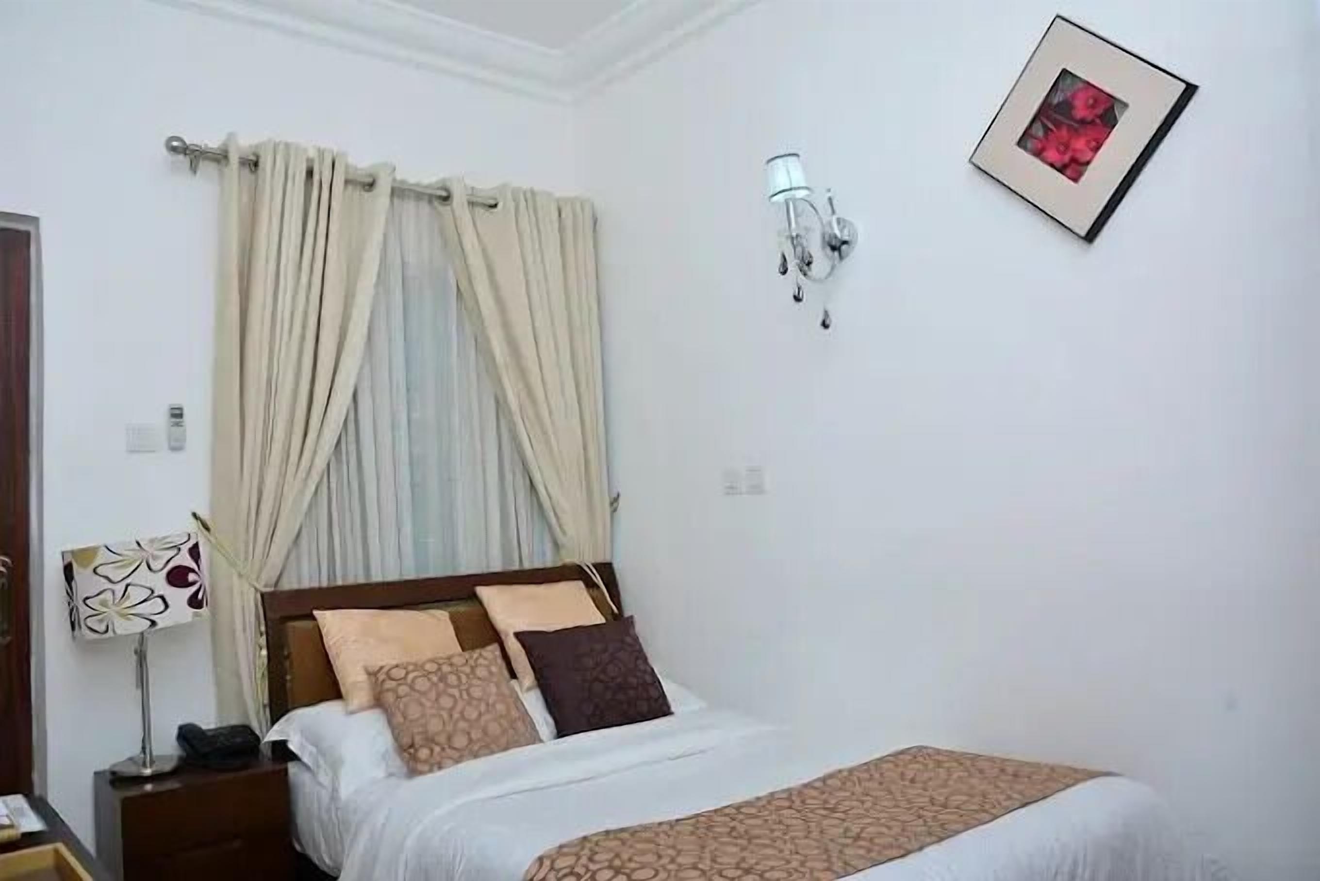A bedroom with a bed, curtains, a wall-mounted lamp, and a framed picture.