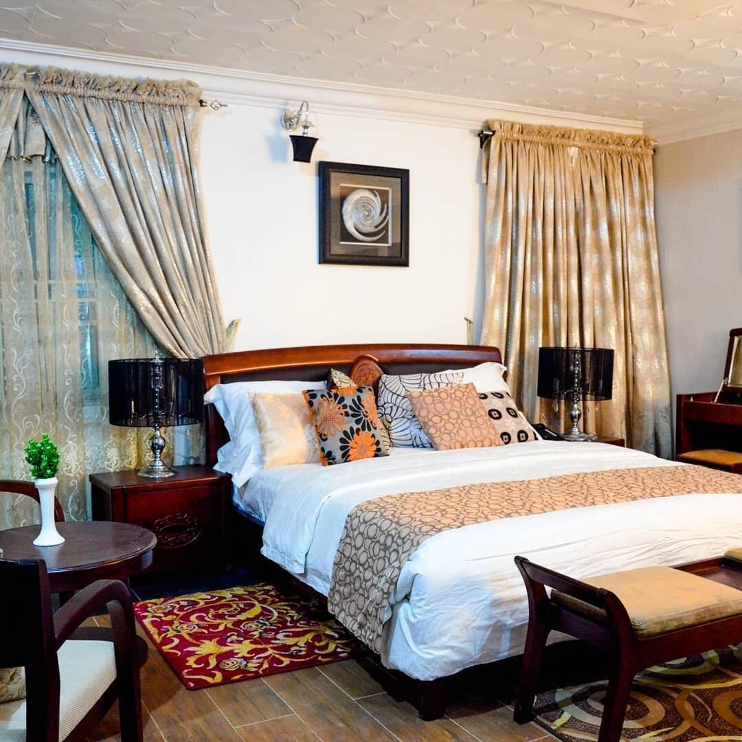 A neatly arranged bedroom with a wooden bed, two bedside tables with lamps, a small round table with a plant, and a patterned rug.