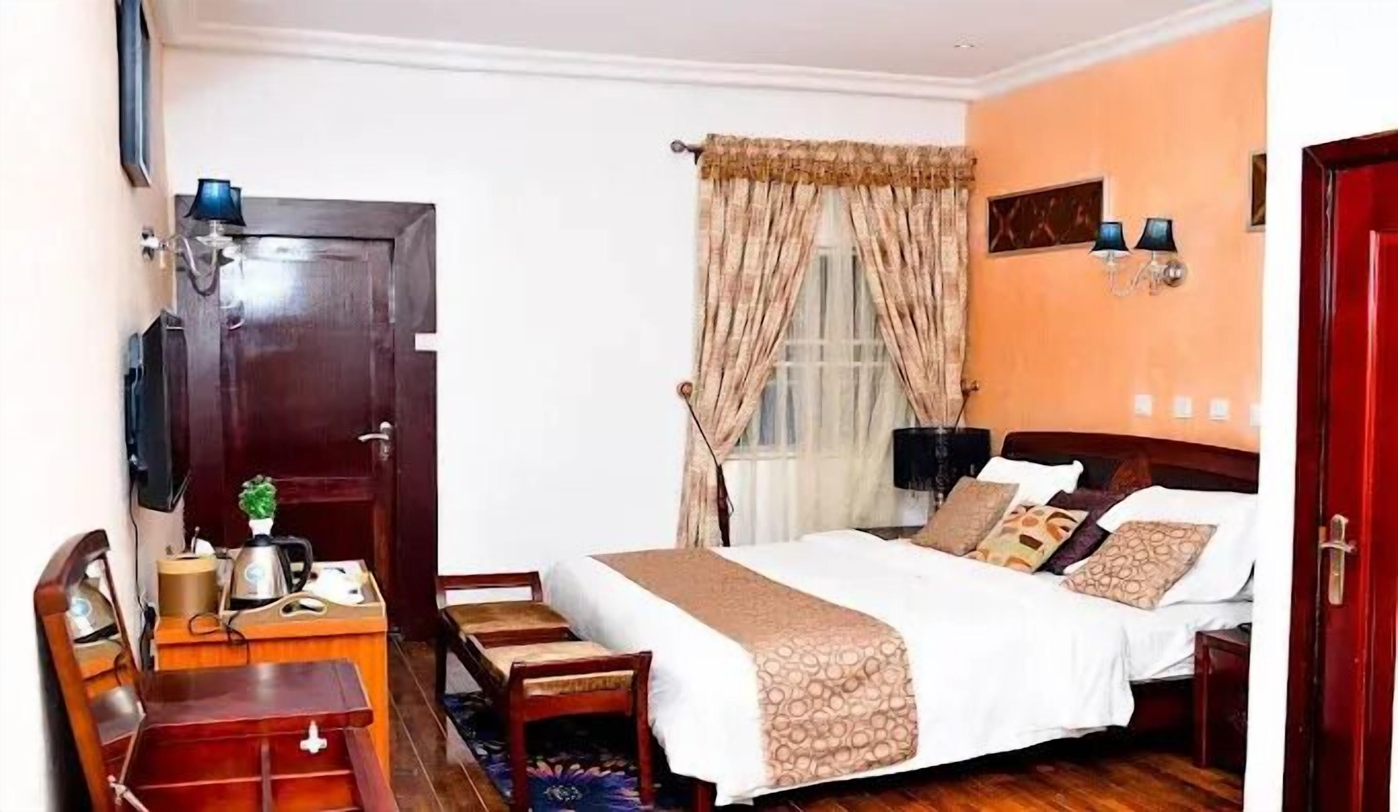Habitación de hotel con cama, mesitas de noche, escritorio, silla, televisión y ventana con cortinas.
