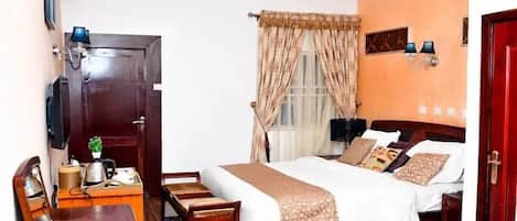 Une chambre d’hôtel comprenant un lit, des tables de chevet, un bureau, une chaise, un téléviseur et une fenêtre avec des rideaux.
