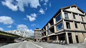 A modern building with multiple balconies and large windows, set against a backdrop of a snow-capped mountain and a clear blue sky. - Gausta Sportell (Tinn)