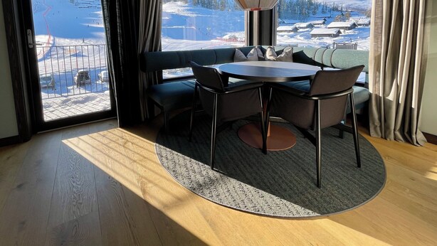 A room with a large window offering a snowy mountain view, a round table with chairs, a sofa, and a hanging light fixture. - Gausta Sportell (Tinn)