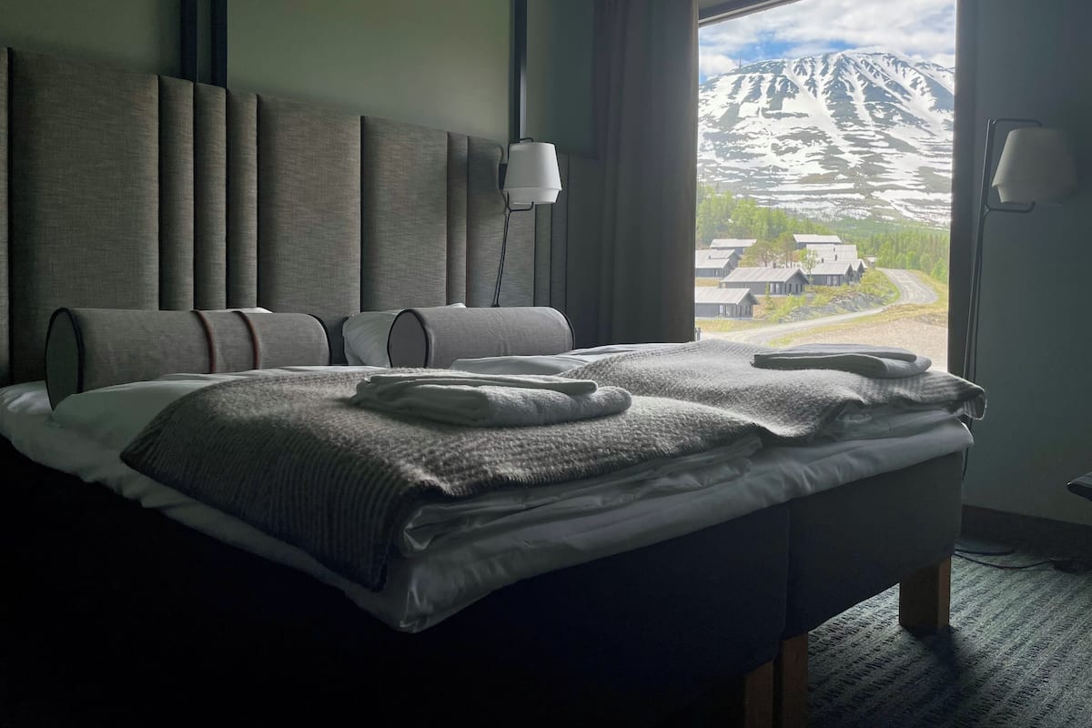 A modern hotel room with a large bed, a view of snow-capped mountains, and a window with curtains.