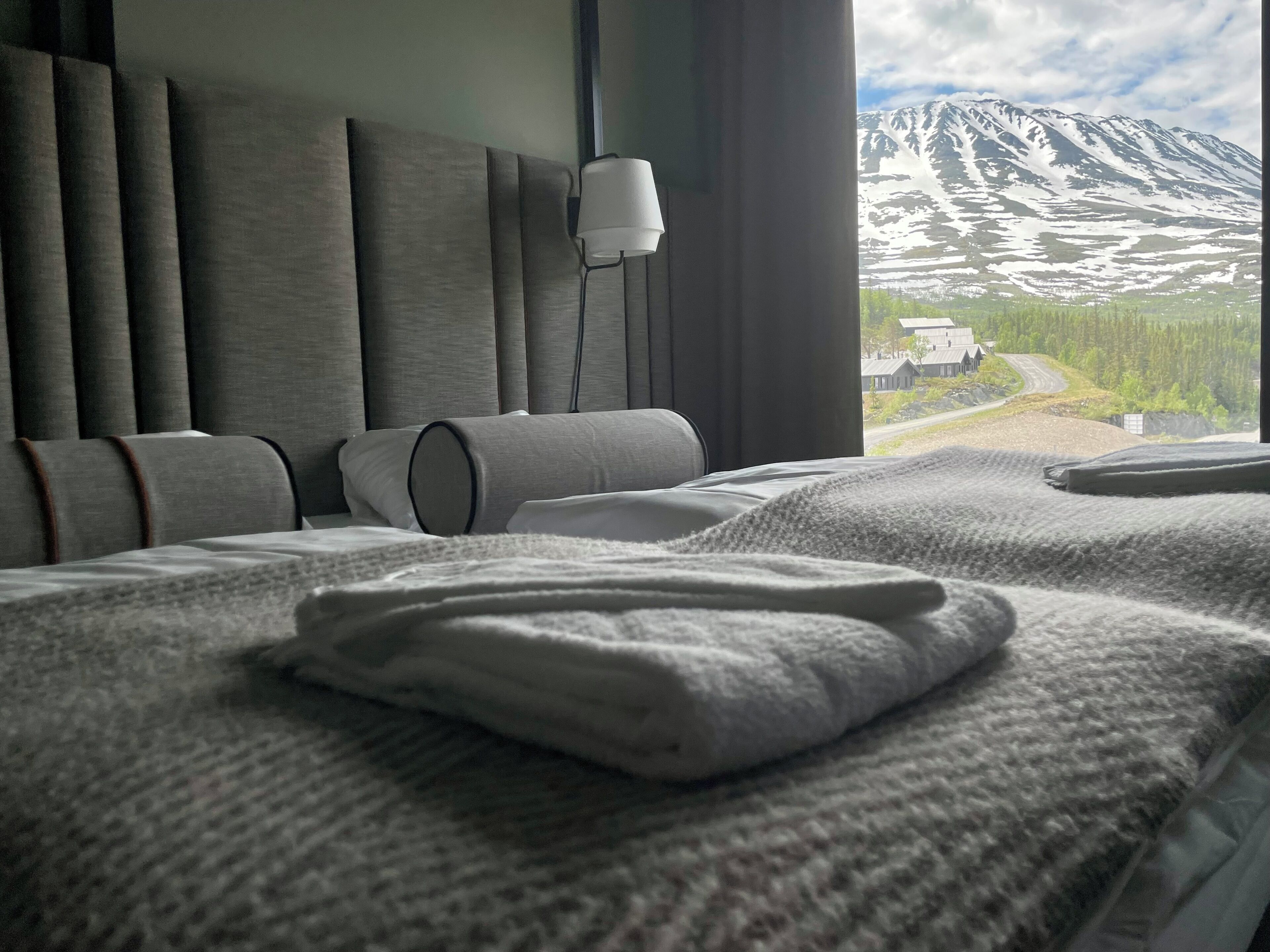 A hotel room with a bed, a bedside lamp, and a view of a mountain landscape.