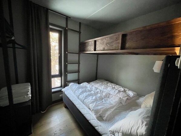 Una habitación pequeña y funcional con una cama litera, un ventanal con vistas y un estante de madera sobre la cama.