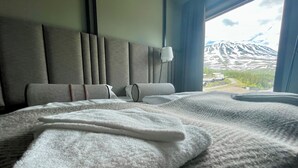 A hotel room with a large bed, a headboard with vertical slats, a bedside lamp, and a view of snow-capped mountains through a window. - Gausta Sportell (Tinn)