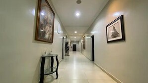 Ein langer, gut beleuchteter Flur mit gerahmten Bildern an den Wänden, ein kleiner Tisch mit einer Lampe und eine Treppe im Hintergrund.