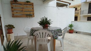 A patio with a table and chairs, potted plants, and a wooden planter wall. - Cozy vacation home in Terrasini a stone's throw from the sea and the historic center. (Terrasini)