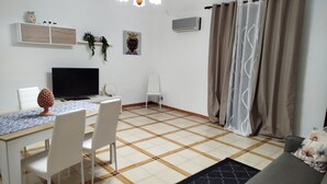 A living room with a TV, white chairs, a dining table, a sofa, and a patterned rug. - Cozy vacation home in Terrasini a stone's throw from the sea and the historic center. (Terrasini)