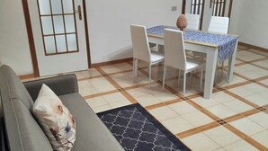 A living room with a sofa, a dining table with chairs, a clock on the wall, and a patterned rug. - Cozy vacation home in Terrasini a stone's throw from the sea and the historic center. (Terrasini)
