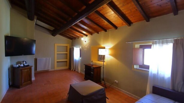 Ein geräumiges Zimmer mit Holzbalkendecke, einem Bett, einem Fernseher, einem Schreibtisch und einem Vorhangfenster.