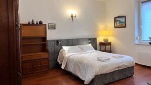 Ein Schlafzimmer mit einem Bett, einem Nachttisch, einer Wandleuchte, einem Bild und einem Holzkabinett.