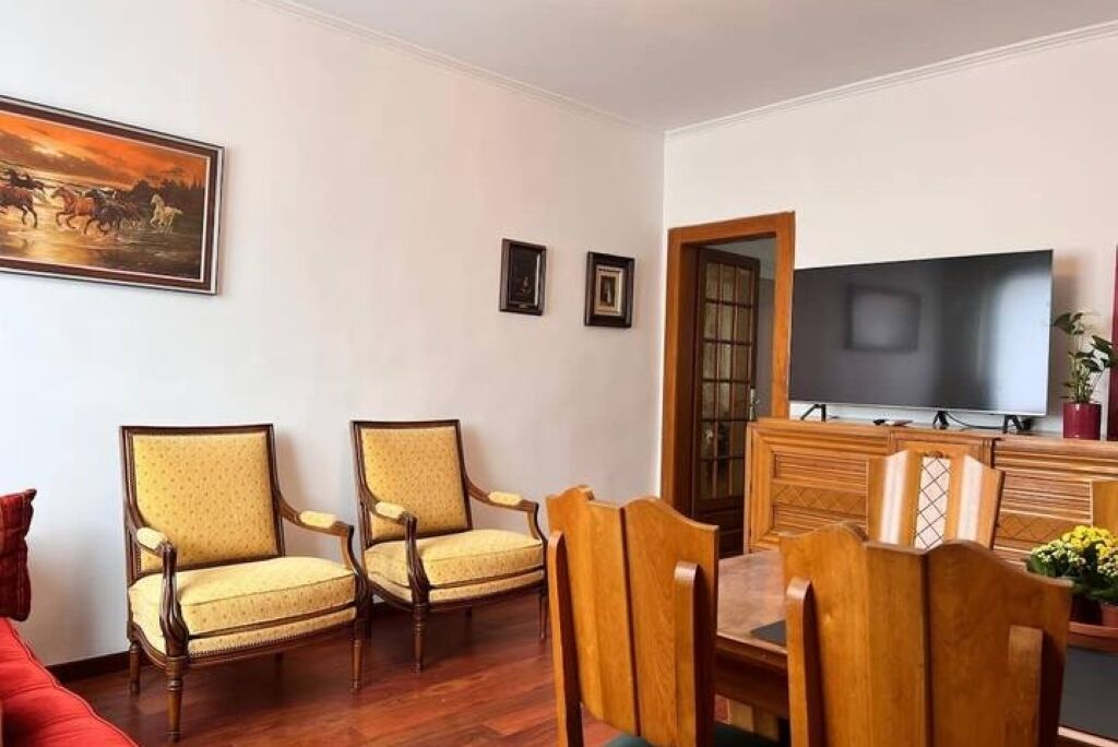 Un salon avec deux fauteuils, une table à manger en bois, un téléviseur à écran plat et un tableau accroché au mur.