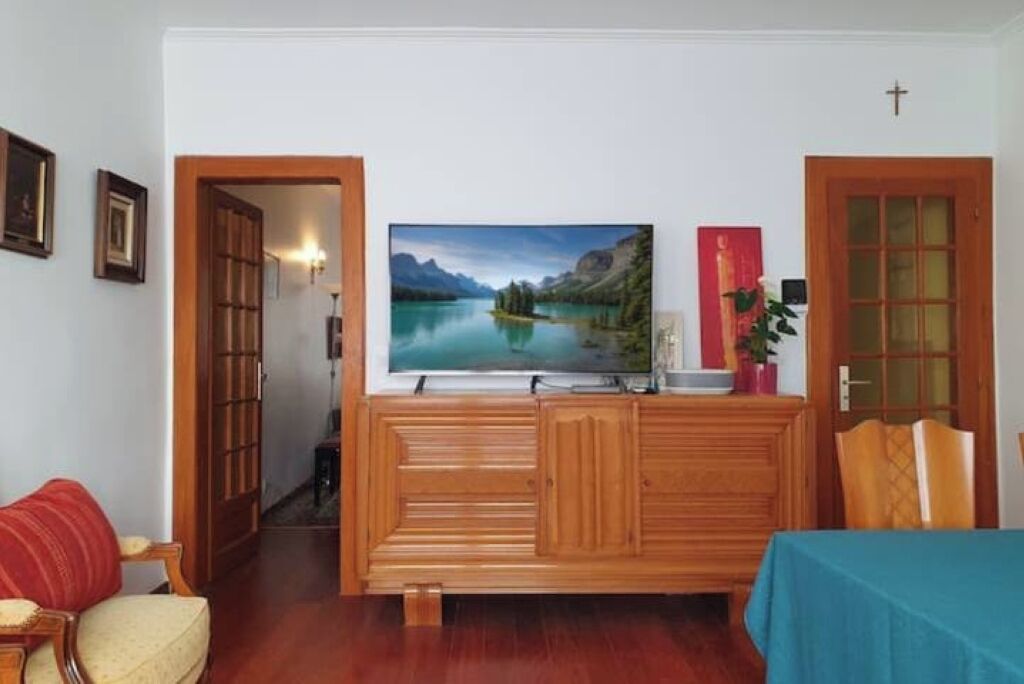 Een woonkamer met een houten kast, een aan de muur bevestigde televisie en een deur met een kruis erboven.