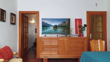 Een woonkamer met een houten kast, een aan de muur bevestigde televisie en een deur met een kruis erboven.