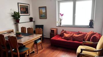 A dining area with a wooden table and chairs, a red sofa, and a window with a view.
