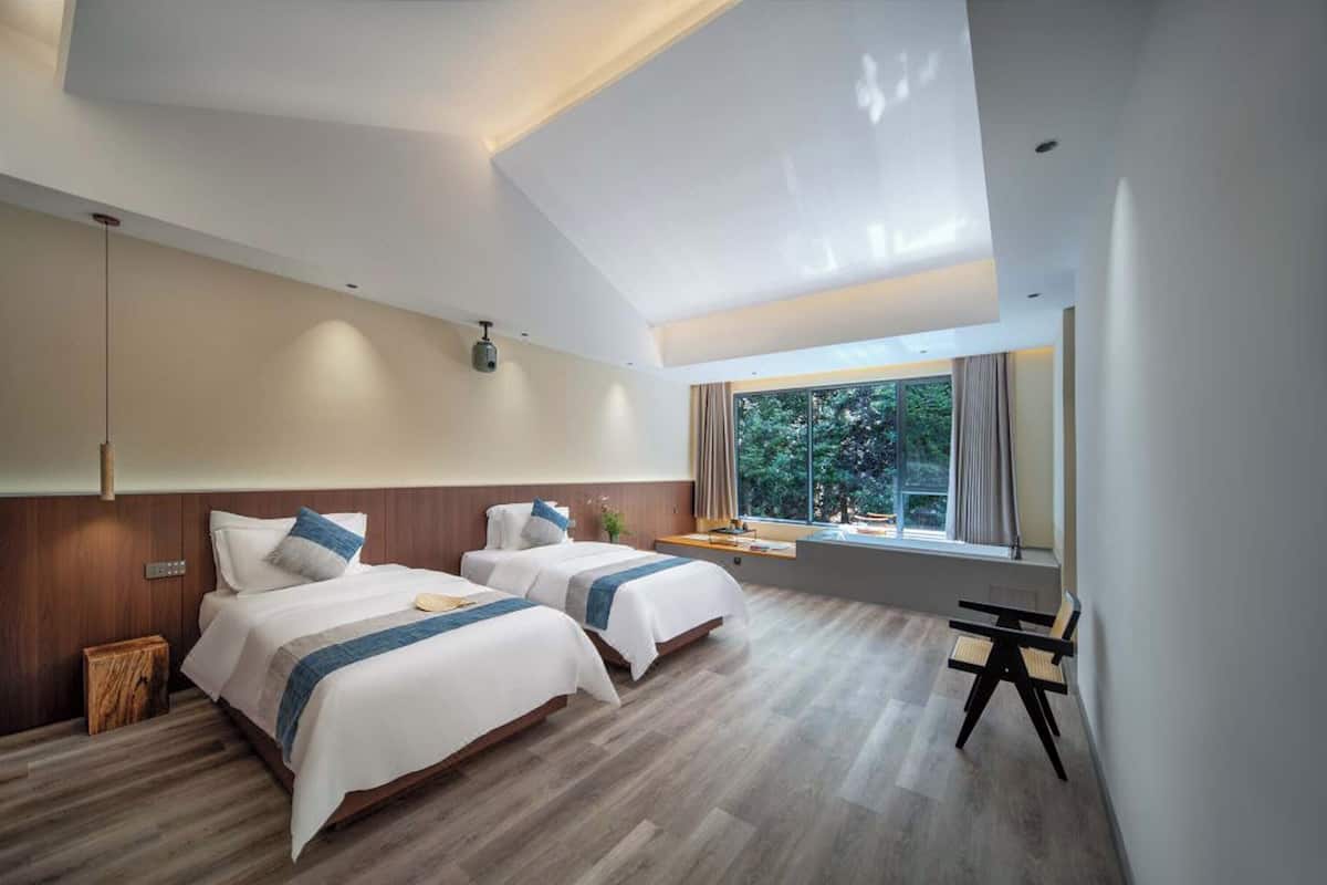 Une chambre d’hôtel moderne avec deux lits, une grande fenêtre et un puits de lumière.