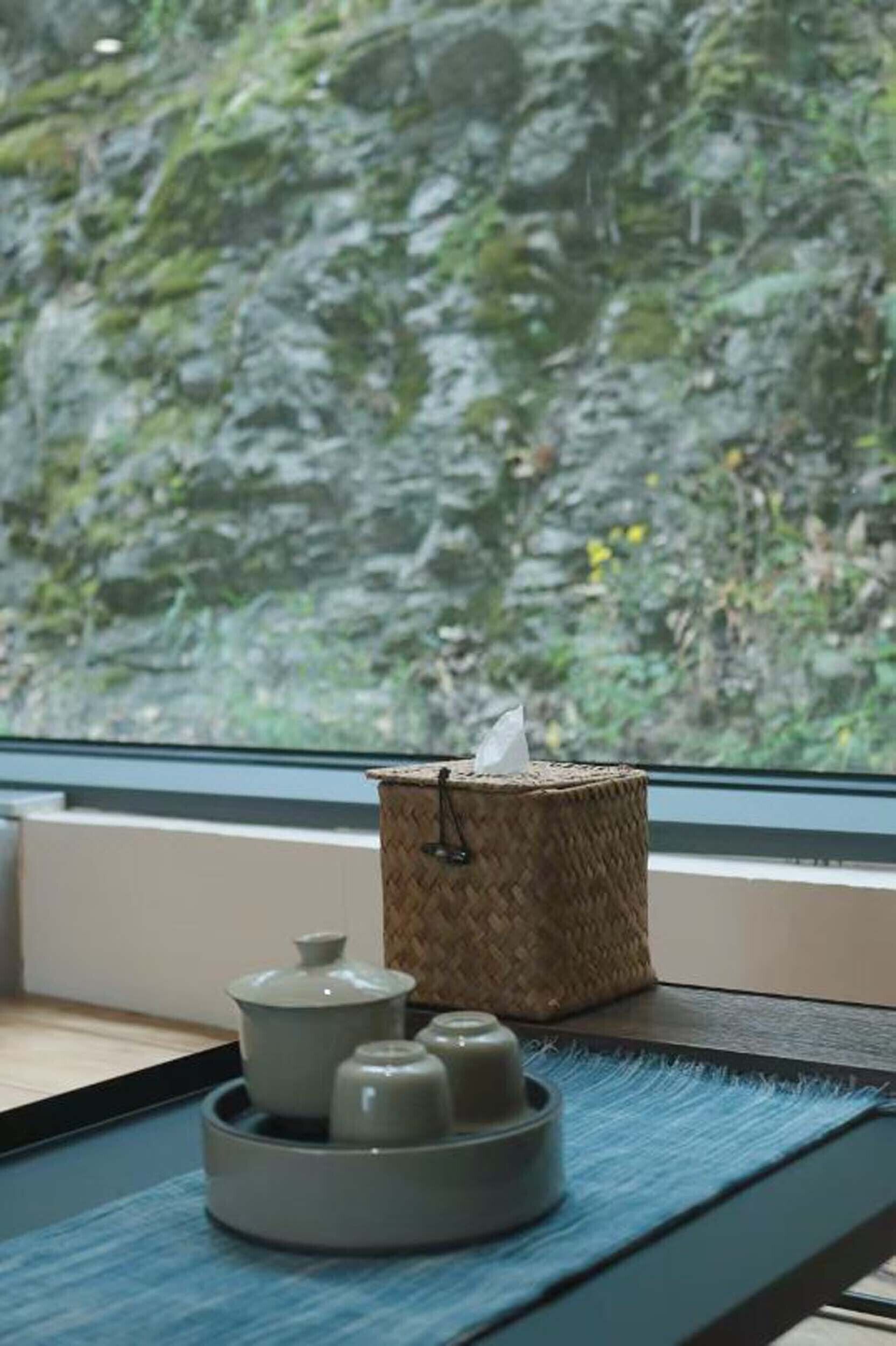 A window view of a rocky landscape with a woven basket and ceramic containers on a tray.