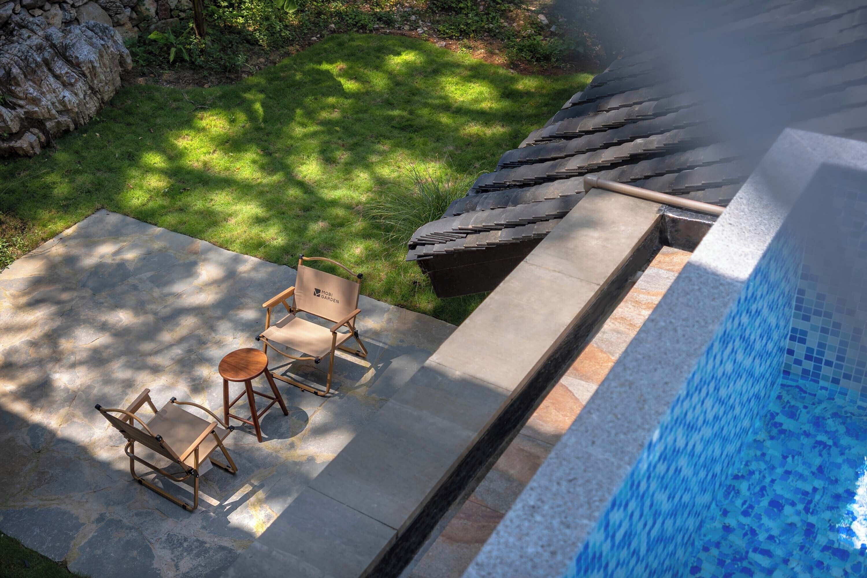Eine Terrasse mit zwei Holzstühlen, einem Steintisch, einem Swimmingpool und einer Steinmauer.