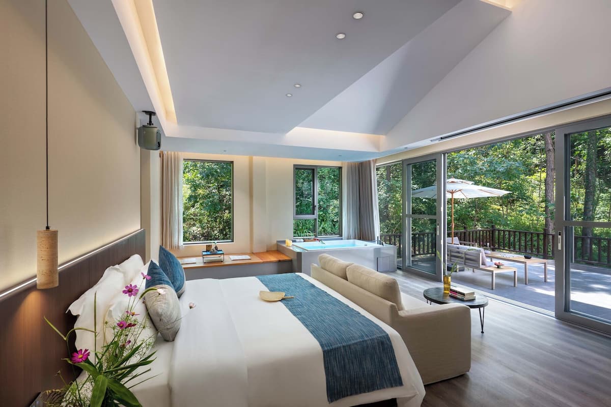 Une chambre d’hôtel moderne, dotée d’un grand lit, d’un canapé, d’une petite table et d’un balcon offrant une vue sur l’extérieur.
