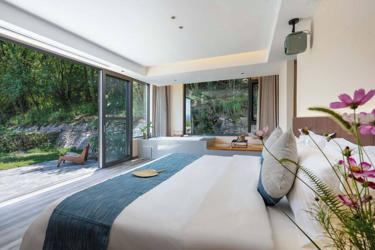 Une chambre moderne avec un grand lit, une vue sur une forêt et un petit coin salon avec une table et des chaises.