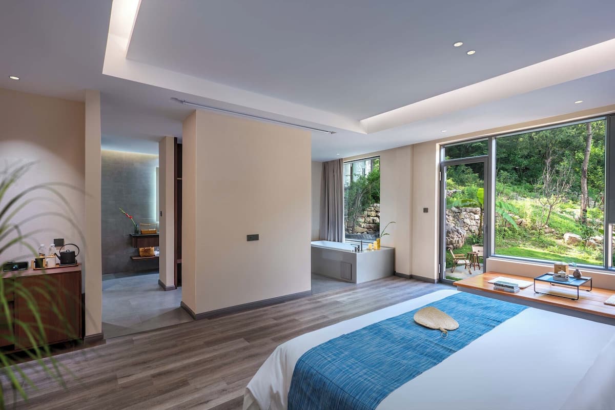 Une chambre moderne avec un grand lit, une vue sur l’extérieur et une salle de bain équipée d’un lavabo et d’un meuble-vasque.