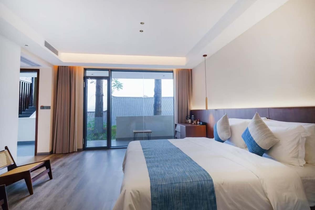 Une chambre d’hôtel avec un grand lit, un bureau, une chaise et une vue sur l’extérieur grâce à une porte coulissante.