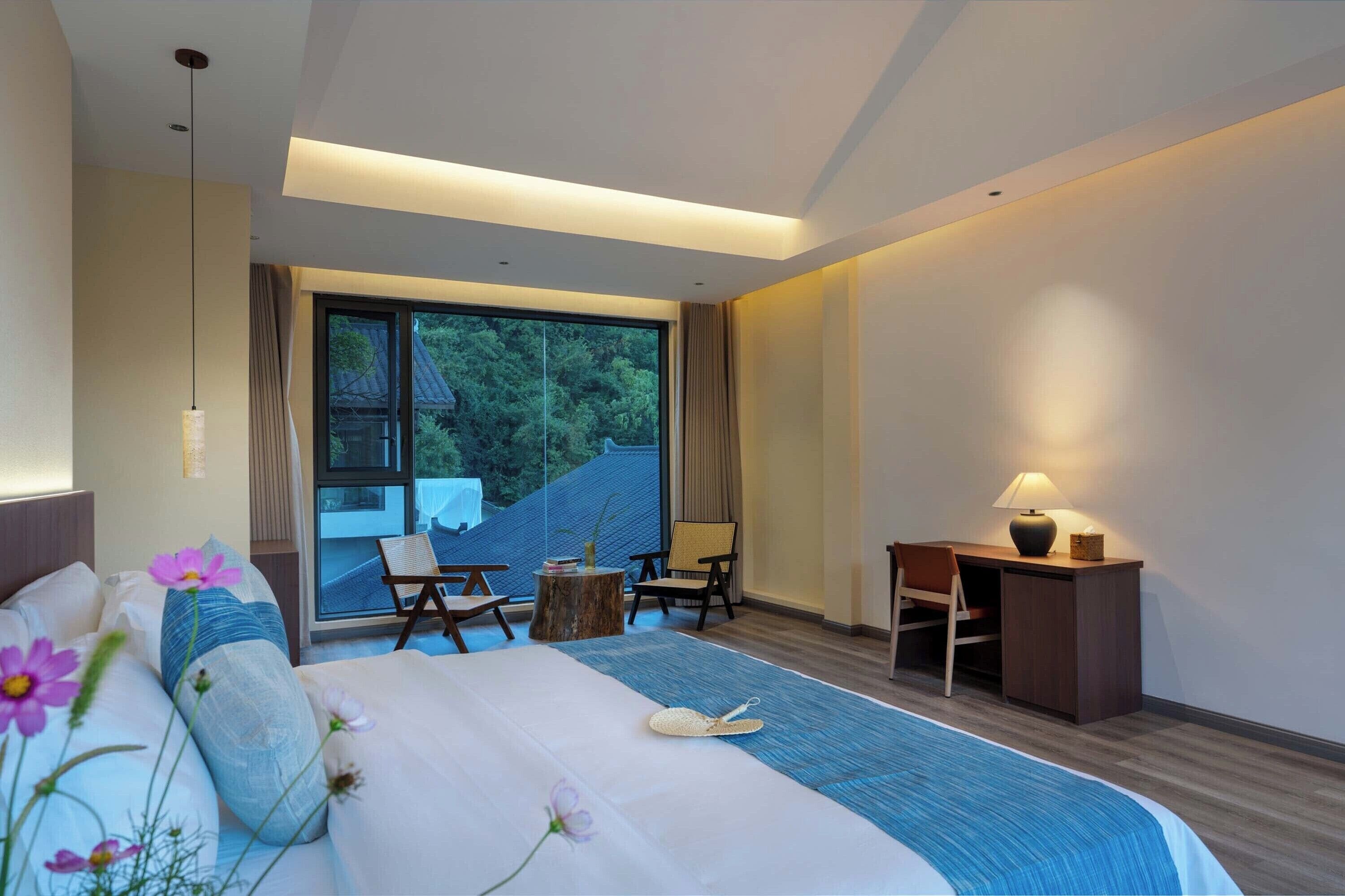 A modern hotel room with a large bed, a desk, and a view of the outdoors.