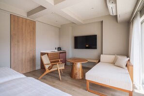 Een moderne hotelkamer met een bed, bank, houten vloer, bureau, stoel, rond houten tafeltje en een aan de muur bevestigde televisie.