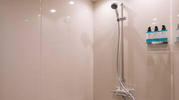 A shower with a handheld showerhead, a wall-mounted control panel, and a shelf with toiletries.