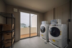 Una sala de lavandería con dos lavadoras, un estante con cestos y una puerta corrediza de vidrio que da a un balcón.